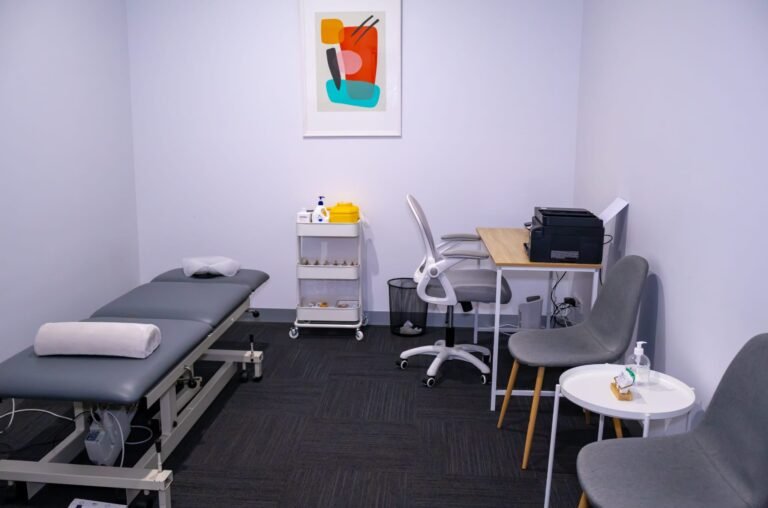 Reservoir clinic treatment room with adjustable physio table, supply cart and abstract art